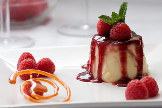 Delicious looking pannacotta pie topped with strawberry sauce and decorated with burned sugar and fresh raspberries