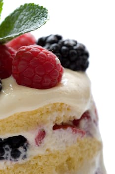 Closeup of dessert made of layers of cake filled with fresh fruits and mascarpone cream, topped with fresh raspberries and blackberries and a mint leave