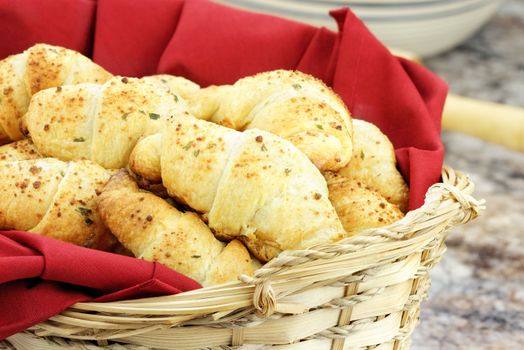 Delicious croissants  brushed with butter, and sprinkled with parmesan cheese and herbs in a wicker basket with mixing bowl and rolling pin in background. Shallow depth of field.