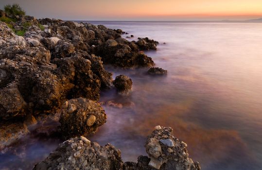 Image shows a serene rocky seascape right after sunset