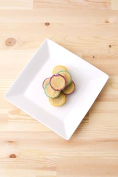 Plate of small undecorated cupcake in multicolored paper cup