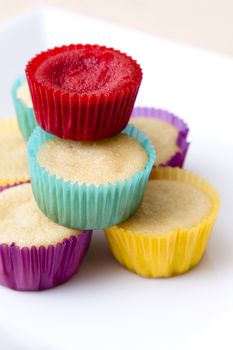 Plate of small undecorated cupcake in multicolored paper cup