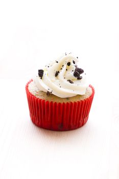 cupcake in red paper cup on a wood table with vanilla icing and cookie crumbs