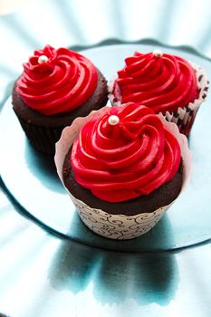 three chocolate cupcake with red icing a pearl on a turquoise plate