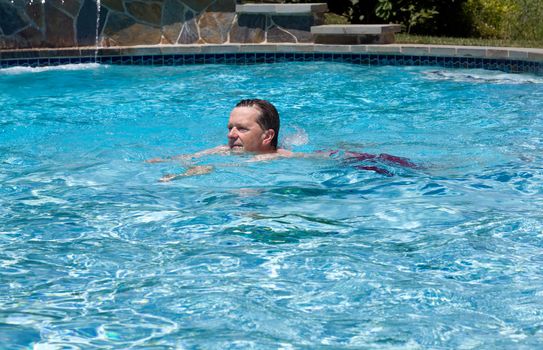 Baby boomer male swimming across a backyard swimming pool on a hot summers day