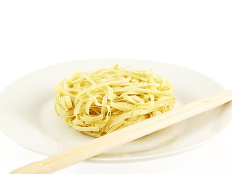 Dried uncoocked noodles, on white plate with chopsticks, isolated towards white background