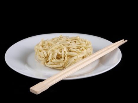 Uncooked noodles, on white plate, with chopsticks, isolated towards black background