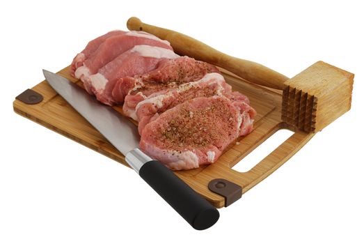 Seasoned chops on bamboo cutting board with chef knife and meat tenderizer mallet isolated on white background