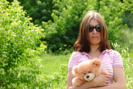 The girl in a sun-protection point on a summer meadow with a bear cub