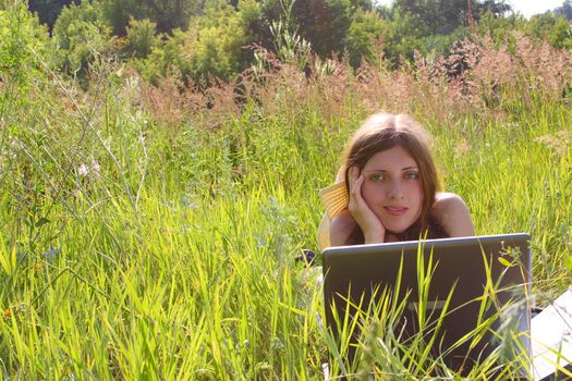 The girl with the laptop, lying on a summer meadow
