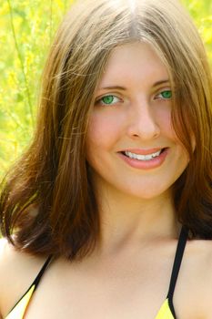 The girl with green eyes in a bathing suit on a blossoming meadow