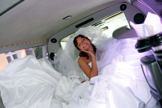 Happy young adult bride in wedding car limousine.