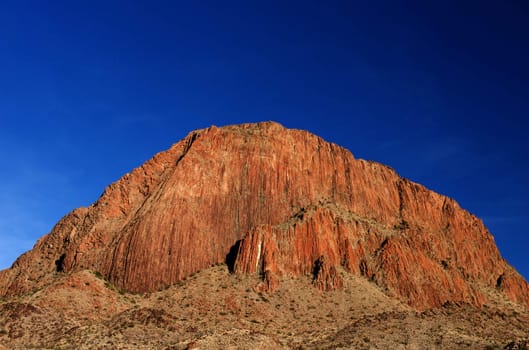 An image of a large red mountain with a blue sky background