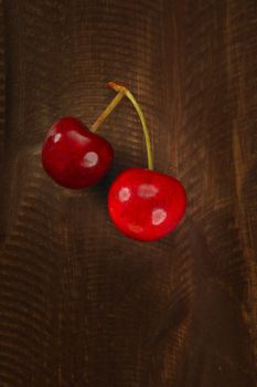 Two cherry red fruits over dark wooden background
