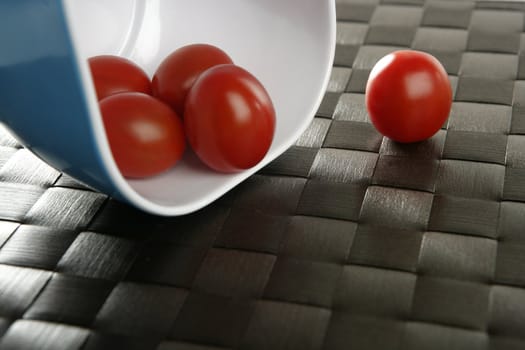 Group of cherry tomatoes falling from blue bowl over brown tablacloth