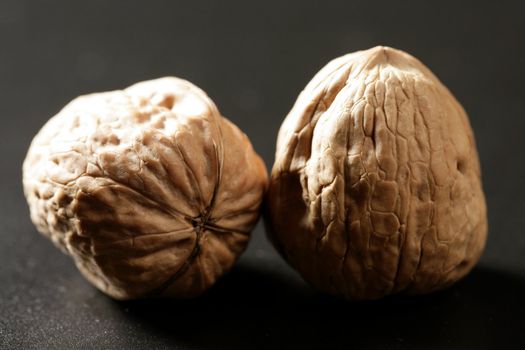 Two walnuts with shells over black background