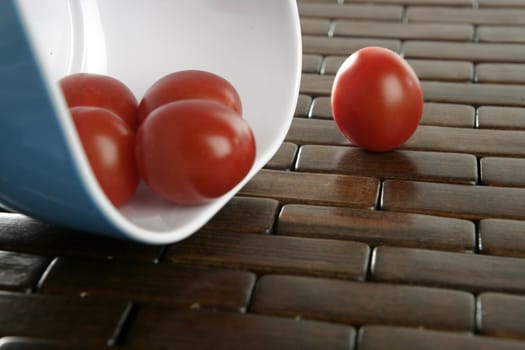 Group of cherry tomatoes falling from blue bowl over brown tablacloth