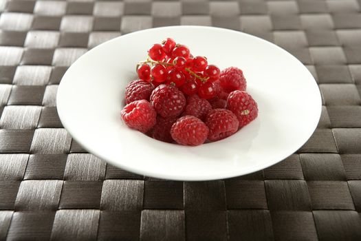 Redcurrant and raspberries in a wite little dish over brown tablecloth