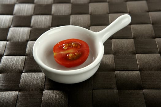 Half cherry tomato in a little dish over brown tablecloth