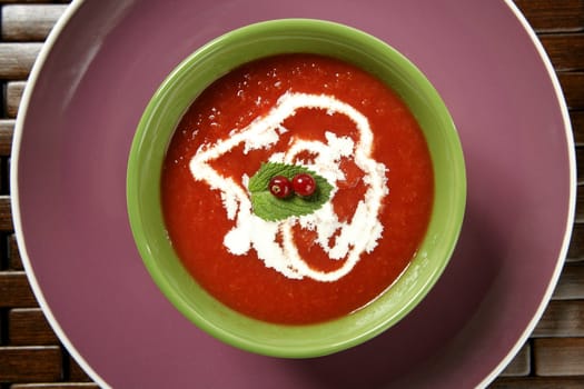 Mediterranean tomato soup with basil and redcurrant in a colorful green dish over wood