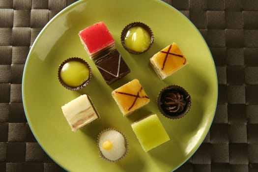 Varied pastries in green dish. Little colorful cakes