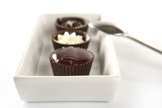 Three little chocolate cakes in a line with cream, strawberry jam and spoon