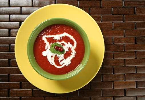 Mediterranean tomato soup with basil and redcurrant in a colorful green dish over wood