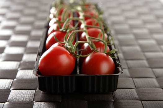 Red tomatoes branch un a black plastic box over brown tablecloth