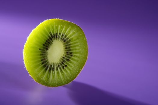 Green Kiwi slice over vivid purple background, copy space