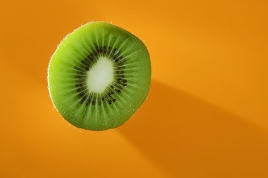 Green Kiwi slice over vivid orange background, copy space
