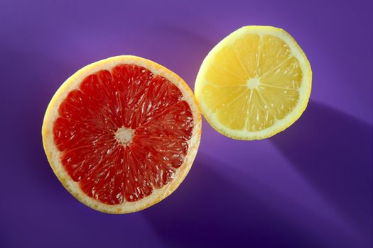 Citrus slices, lemon and grapefruit fruits over purple background