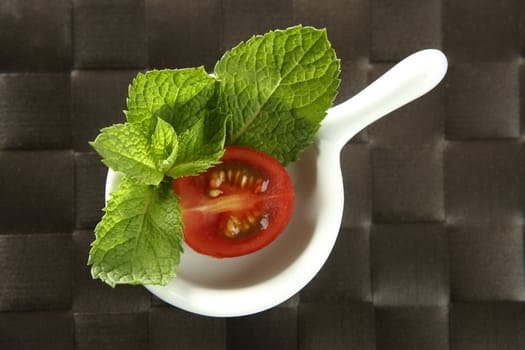 Half cherry tomato in a little dish over brown tablecloth and basil leaves arround