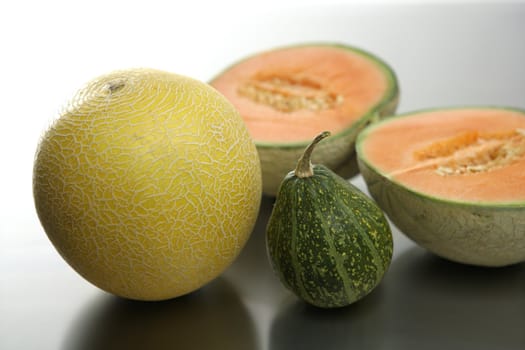 Two melon fruit over a stainless steel table and little green pumpkin