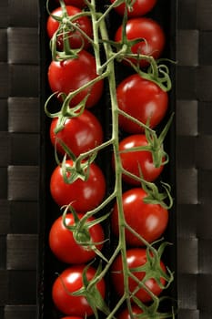 Red tomatoes branch un a black plastic box over brown tablecloth