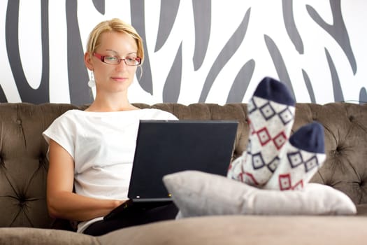 Relaxed, beautiful young woman sitting on sofa, using netbook