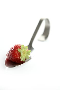 Strawberry in a curved stailess steel spoon. White studio background