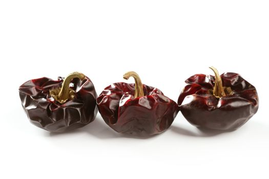 Three round Mediterranean dried dark red peppers over white at studio, isolated