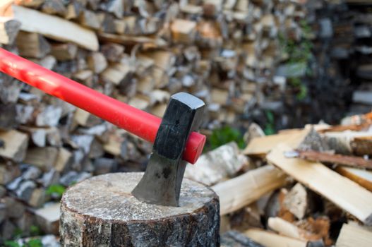 Axe thrust in a birch chock against  woodpile of fire wood.