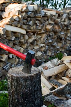 Axe thrust in a birch chock against  woodpile of fire wood.