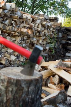 Axe thrust in a birch chock against  woodpile of fire wood. Focus on a woodpile