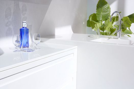 White modern kitchen detail, blue water bottle and green plants