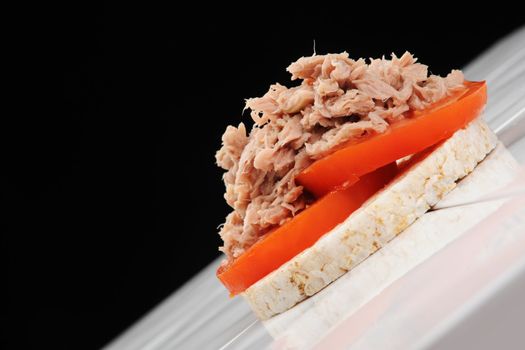 Tuna and Tomato on Rice cake on a ceramic table, shot against black at an angle.