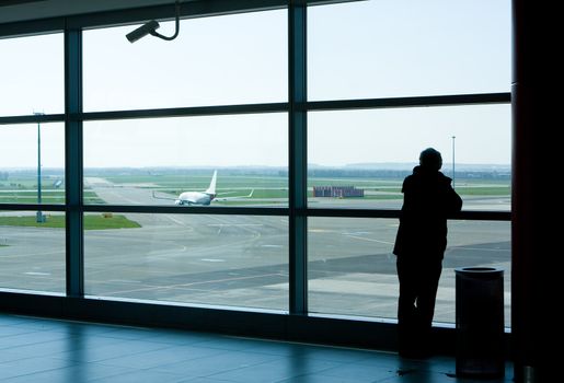 Airport lounge or waiting area with business man standing looking outside of window towards control tower