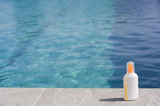 Sun tan lotion at poolside against turquoise water background