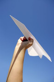 Paper airplane in children hand over sunny summer blue sky