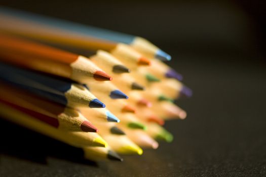 Close up of group of multi-colored coloring pencils isolated on blsck background.