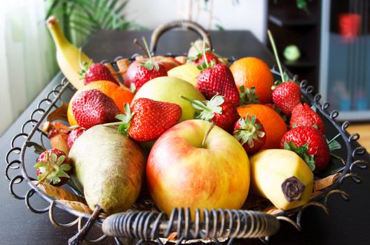 fruits basket in living room with strawberries, apples, pears, oranges, lemon, bananas