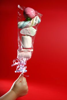 children hand with a stick full of sweet candy over red background