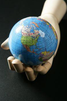 The world map in a wooden mannequin hand, black backgorund