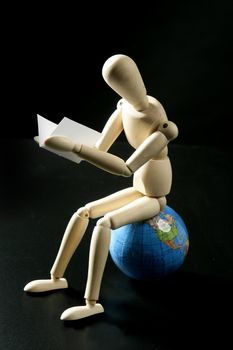 Wooden little mannequin sitting over the world map, reading and learning student